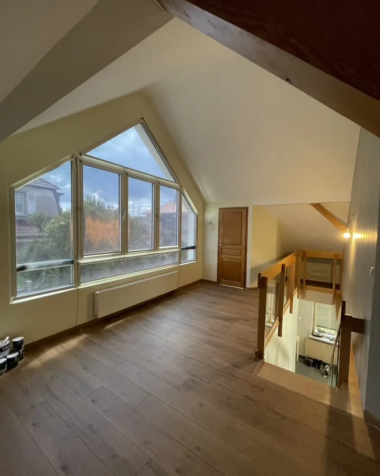 Pièce sous combles avec grande fenêtre triangulaire et sol en bois clair